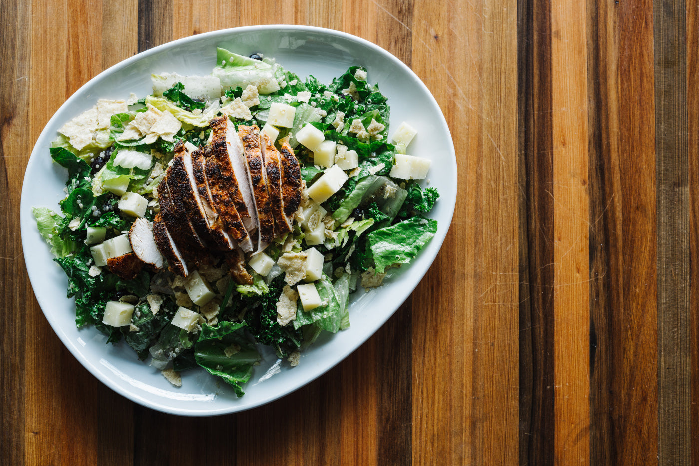 A salad with a piece of grilled chicken on top. 