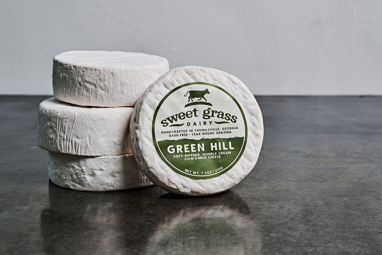 Camembert style cheese named Green Hill stacked to show off the packaging. 