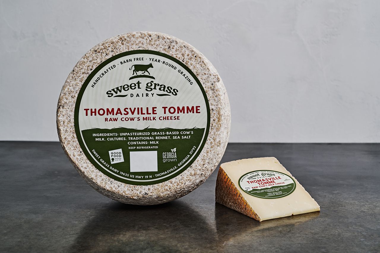 Sweet Grass Dairy's Thomasville Tomme positioned to show a piece of cheese and a wheel of cheese. 