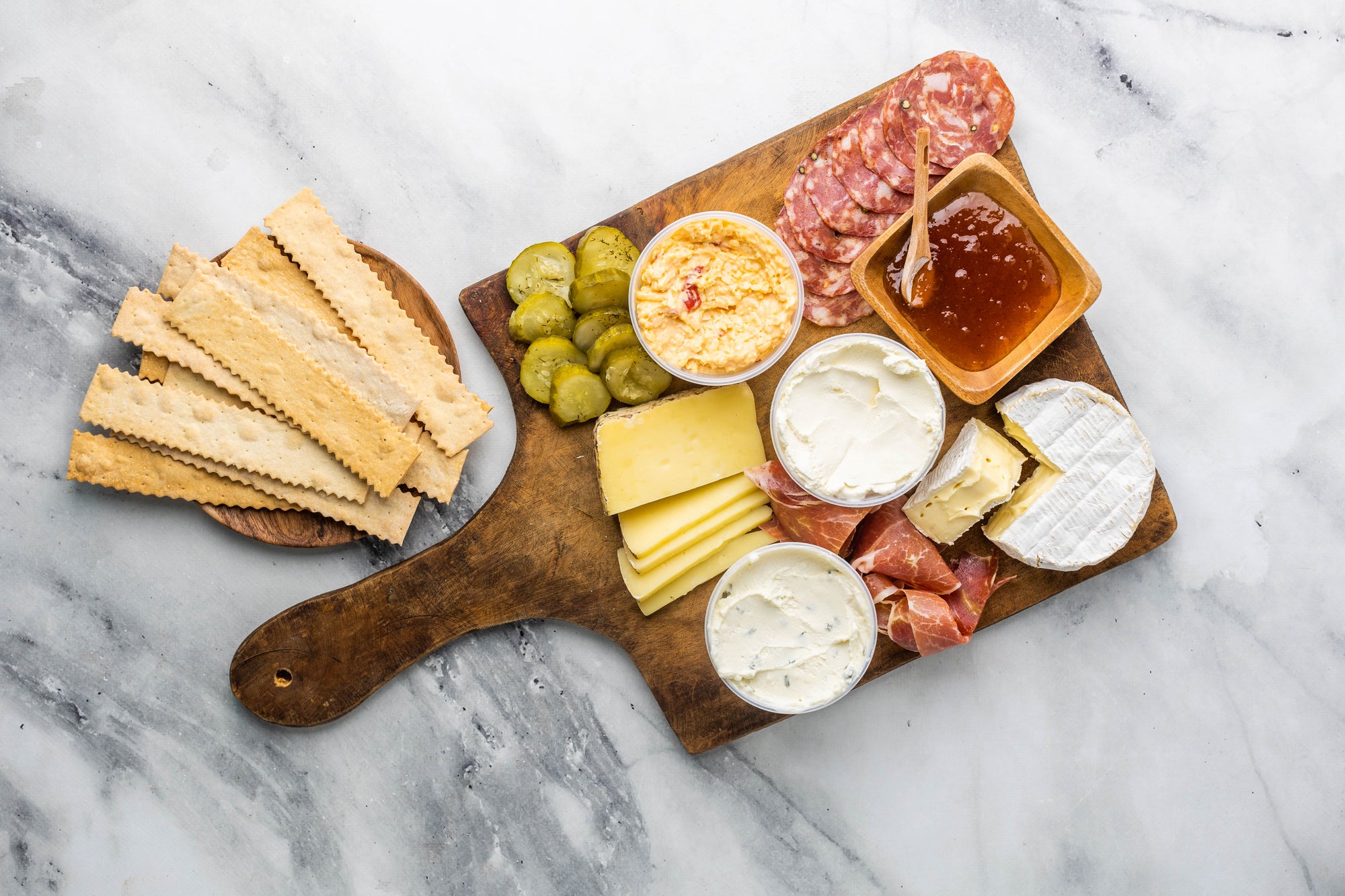 Cheese, Pickles, Salami, Prosciutto, Jam, and crackers on a cheese board ready to eat. 