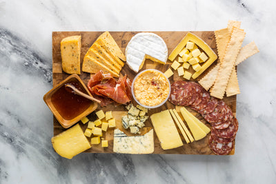 Lots of Cheese, Salami, Prosciutto, Jam, and Crackers on a cheese board ready to eat.